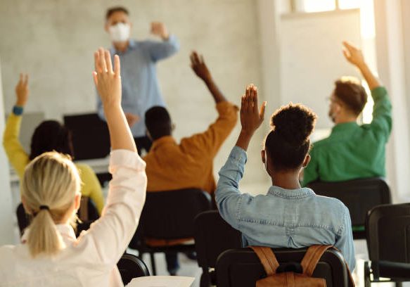 Rear view of college students raising hands to answer teacher's question during a lecture.